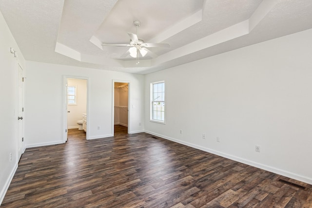 unfurnished bedroom featuring visible vents, baseboards, a raised ceiling, a walk in closet, and dark wood-type flooring