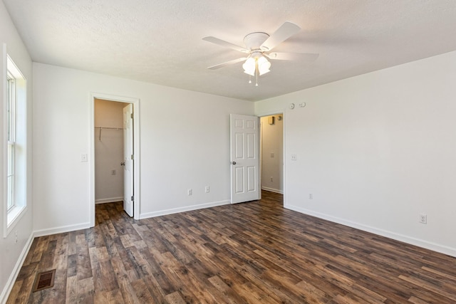 unfurnished bedroom featuring a walk in closet, visible vents, baseboards, and dark wood-style floors