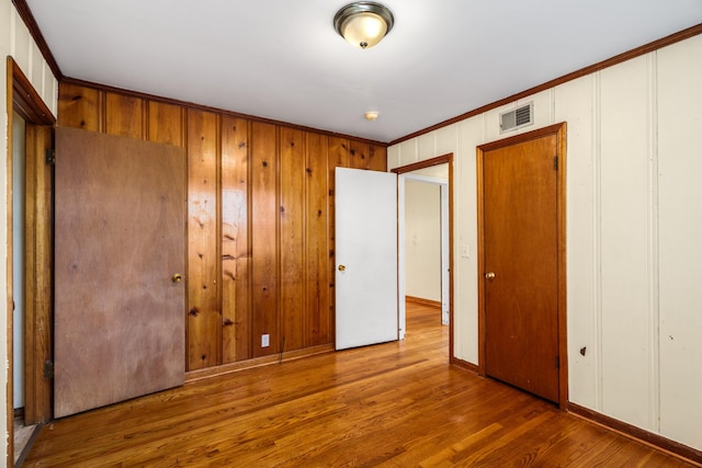 unfurnished bedroom with a closet, wood finished floors, ornamental molding, and baseboards