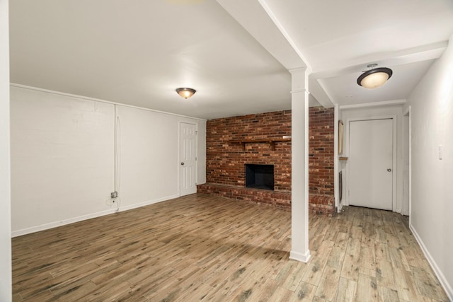 unfurnished living room featuring a fireplace, light wood finished floors, baseboards, and brick wall