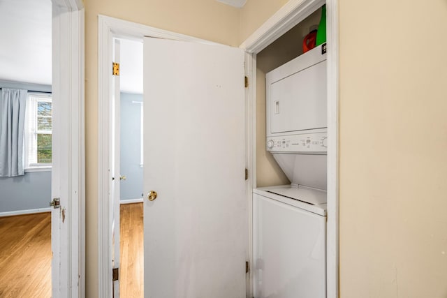 washroom with stacked washing machine and dryer, light wood-type flooring, and baseboards