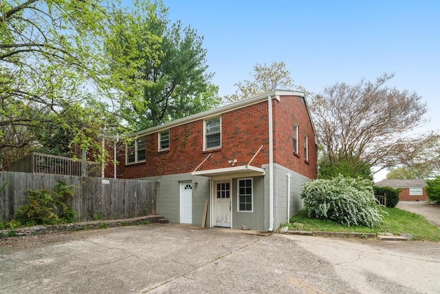 rear view of house featuring fence, brick siding, and concrete driveway