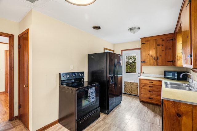 kitchen featuring black appliances, a sink, brown cabinetry, light countertops, and baseboards