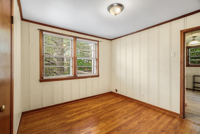 empty room featuring wood finished floors, ornamental molding, and baseboards