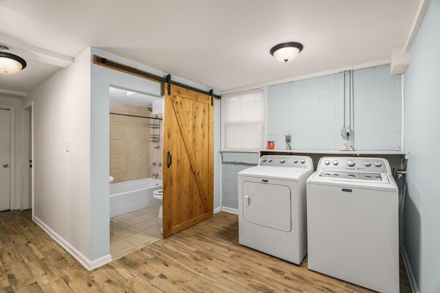 laundry area with washing machine and dryer, light wood finished floors, a barn door, and baseboards