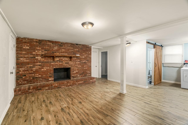 unfurnished living room with washer / dryer, wood finished floors, a barn door, and baseboards