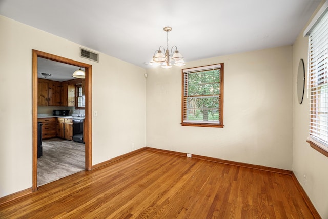 empty room featuring light wood-type flooring, a chandelier, and baseboards
