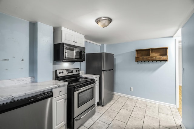 kitchen featuring appliances with stainless steel finishes, white cabinetry, light stone counters, light tile patterned flooring, and baseboards