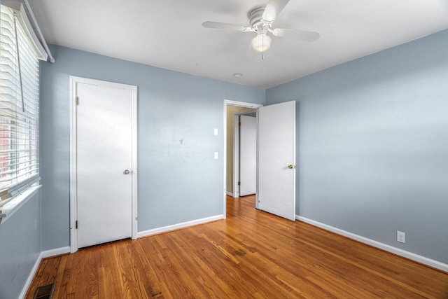 unfurnished bedroom with baseboards, multiple windows, wood finished floors, and ceiling fan