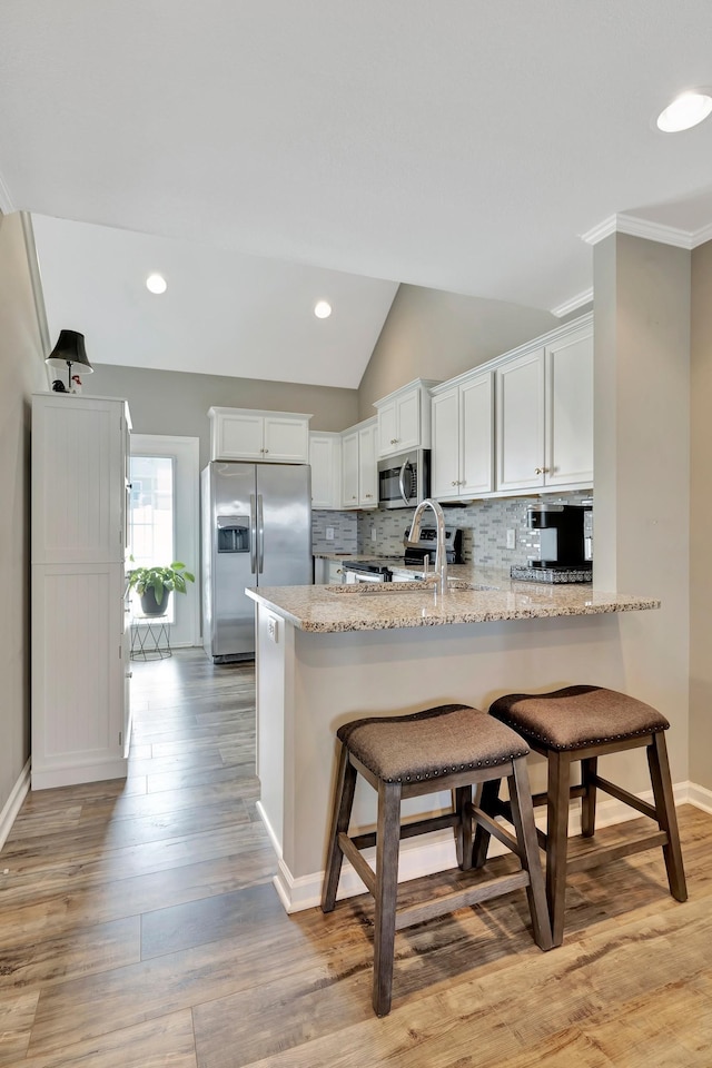 kitchen featuring appliances with stainless steel finishes, a peninsula, white cabinetry, decorative backsplash, and light stone counters