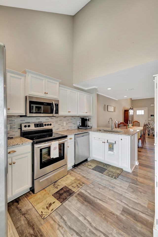 kitchen featuring a peninsula, light wood-style floors, white cabinetry, a towering ceiling, and stainless steel appliances