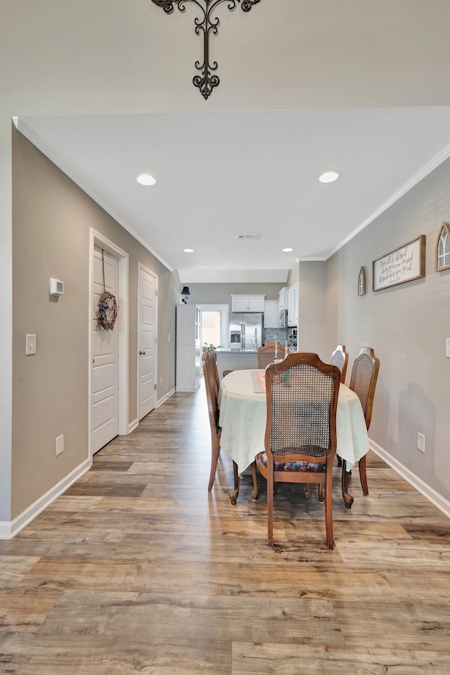 dining space with light wood-type flooring, baseboards, and crown molding