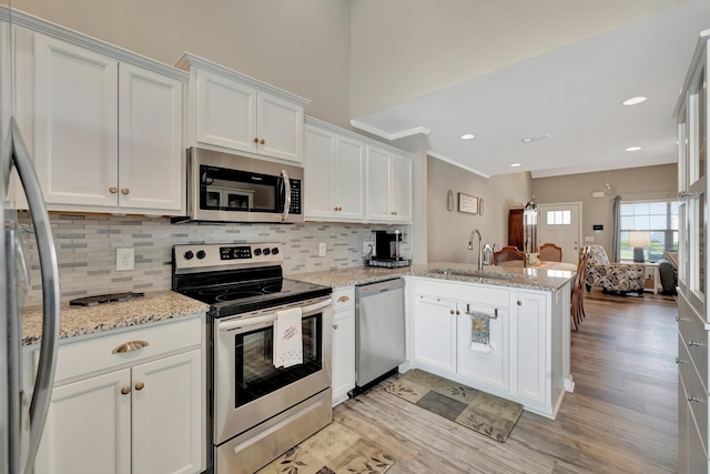 kitchen with a sink, appliances with stainless steel finishes, a peninsula, light wood finished floors, and white cabinetry