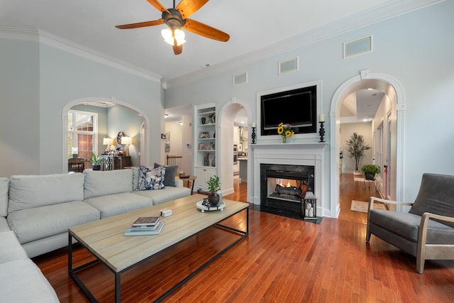 living room featuring arched walkways, visible vents, ceiling fan, a fireplace, and ornamental molding