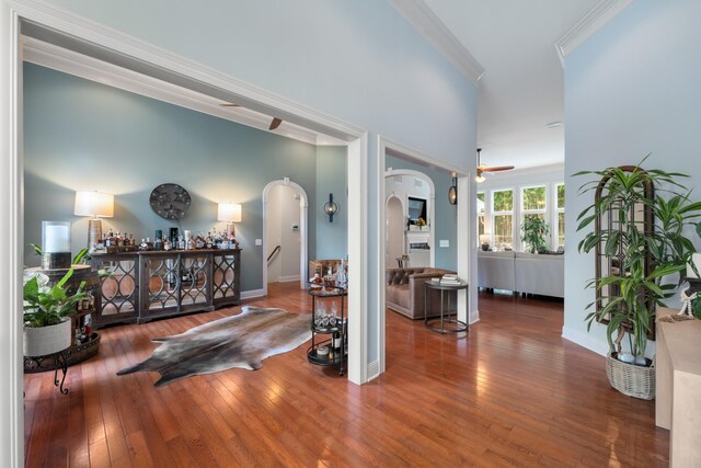 foyer featuring arched walkways, crown molding, a ceiling fan, and wood-type flooring