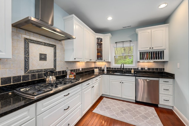 kitchen featuring wall chimney range hood, a sink, stainless steel appliances, decorative backsplash, and dark wood-style floors