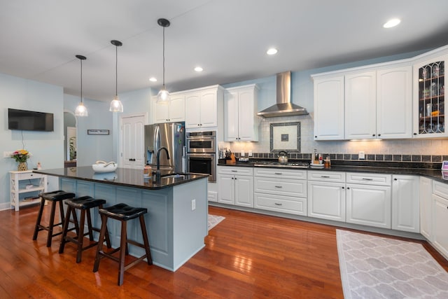 kitchen with appliances with stainless steel finishes, dark wood-style flooring, wall chimney range hood, and dark countertops