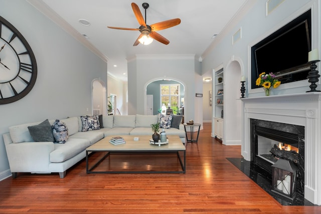 living room featuring a fireplace, a ceiling fan, crown molding, arched walkways, and wood finished floors