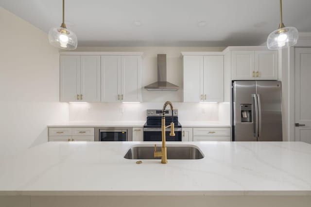 kitchen with stainless steel appliances, white cabinets, wall chimney exhaust hood, and hanging light fixtures