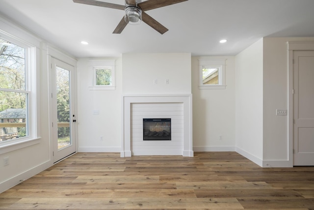unfurnished living room featuring baseboards, a ceiling fan, a glass covered fireplace, and wood finished floors