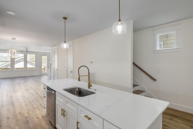 kitchen featuring light wood-style flooring, white cabinets, stainless steel dishwasher, a sink, and hanging light fixtures