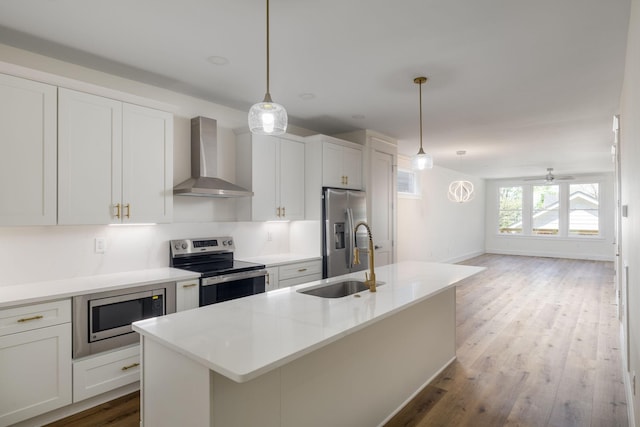 kitchen with wall chimney exhaust hood, a sink, white cabinetry, wood finished floors, and stainless steel appliances
