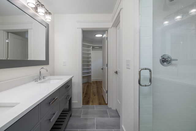 full bath featuring a shower stall, a spacious closet, a sink, tile patterned floors, and double vanity