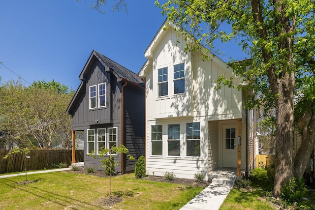 view of front of house with board and batten siding, a front lawn, and fence