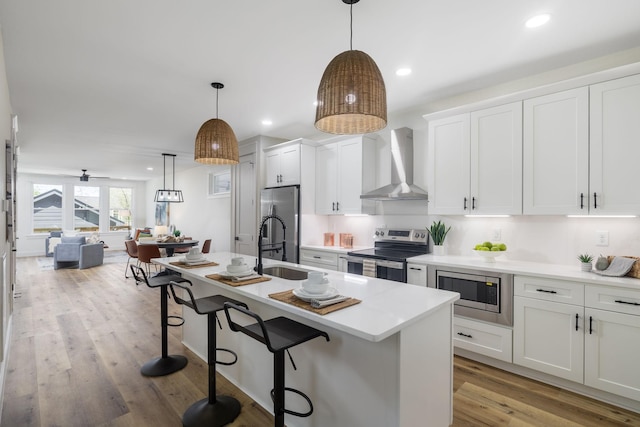kitchen with white cabinets, wall chimney exhaust hood, a kitchen bar, and stainless steel appliances