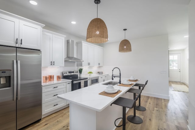 kitchen featuring a sink, wall chimney range hood, light countertops, appliances with stainless steel finishes, and a kitchen island with sink