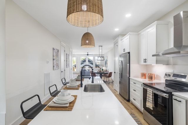 kitchen with light countertops, white cabinets, wall chimney exhaust hood, stainless steel appliances, and a sink