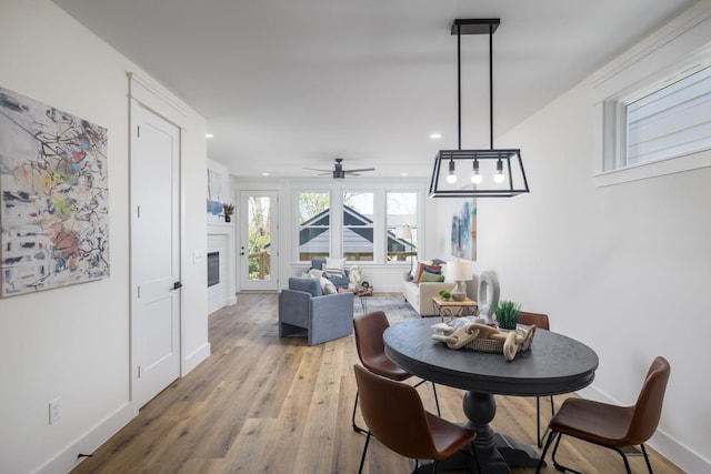 dining room featuring baseboards, ceiling fan, light wood-type flooring, recessed lighting, and a glass covered fireplace