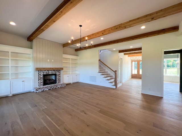 unfurnished living room with french doors, stairs, a brick fireplace, beam ceiling, and wood finished floors