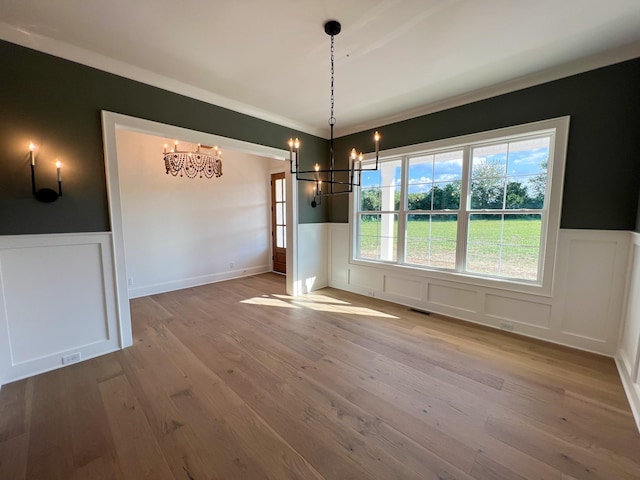 unfurnished dining area with a decorative wall, a wainscoted wall, hardwood / wood-style floors, and an inviting chandelier