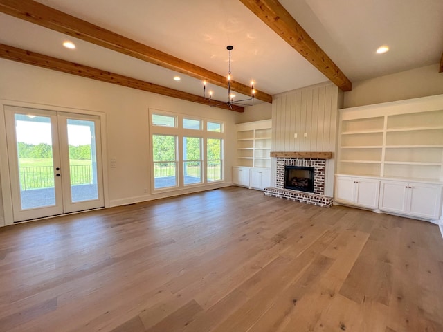 unfurnished living room featuring a brick fireplace, beam ceiling, recessed lighting, light wood finished floors, and french doors