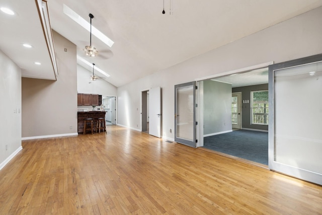 unfurnished living room with a skylight, baseboards, high vaulted ceiling, and light wood-style floors