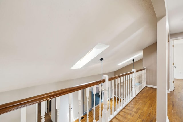 hall featuring baseboards, wood finished floors, and a skylight