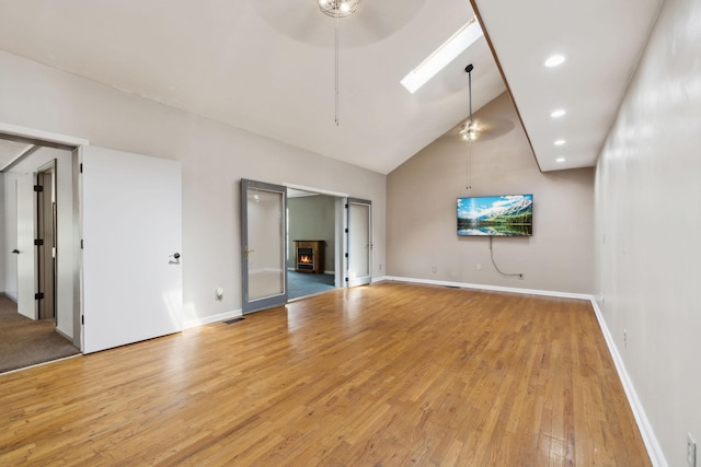 empty room with a warm lit fireplace, a ceiling fan, light wood-style floors, a skylight, and baseboards