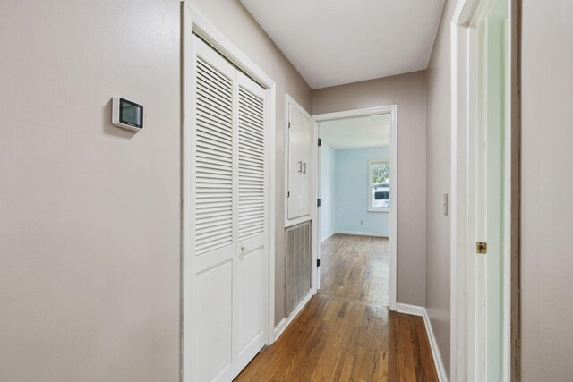 corridor featuring visible vents, baseboards, and wood finished floors