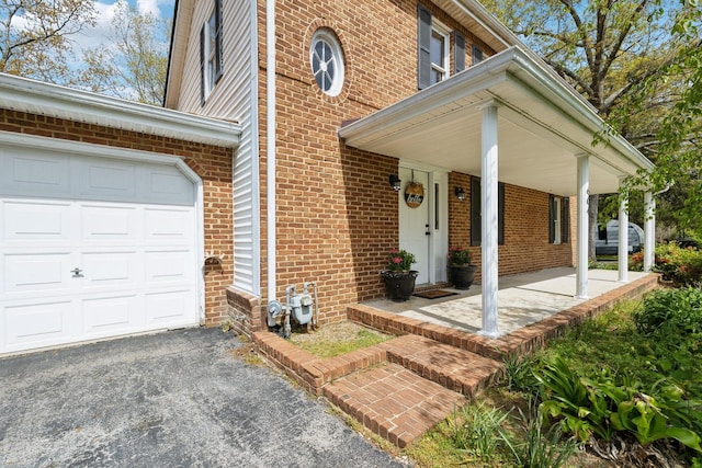 view of exterior entry featuring brick siding, a porch, and a garage