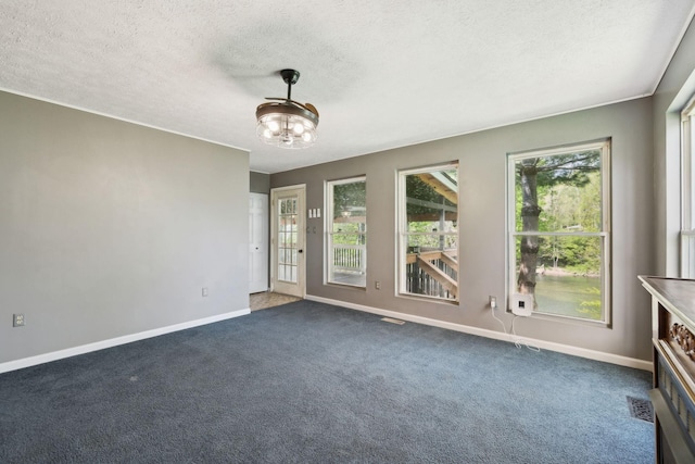 empty room with visible vents, dark colored carpet, baseboards, and a textured ceiling