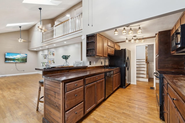 kitchen with a sink, light wood-style floors, open shelves, a breakfast bar, and black appliances