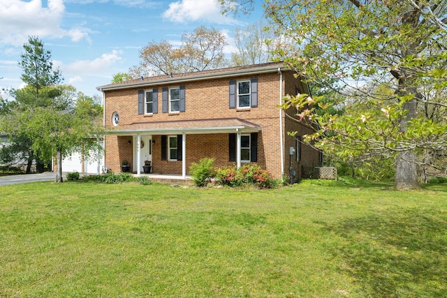 traditional-style home featuring a front lawn, covered porch, brick siding, an attached garage, and aphalt driveway