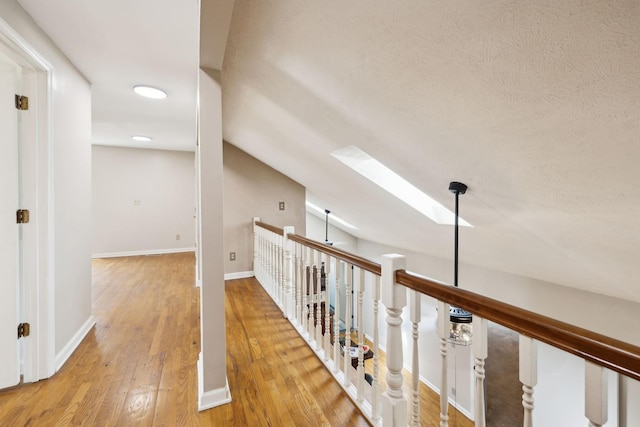 hallway with lofted ceiling with skylight, wood finished floors, a textured ceiling, and baseboards