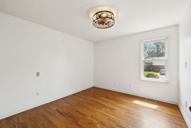 unfurnished room with baseboards, wood finished floors, and visible vents