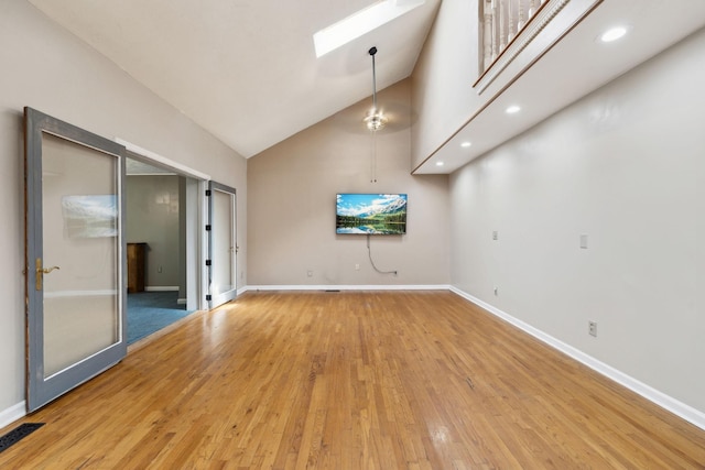 interior space with light wood-type flooring, baseboards, visible vents, a skylight, and high vaulted ceiling