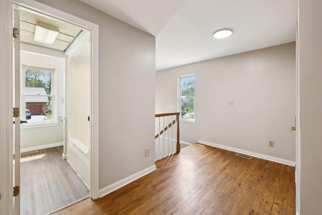 corridor with baseboards, wood finished floors, an upstairs landing, and visible vents