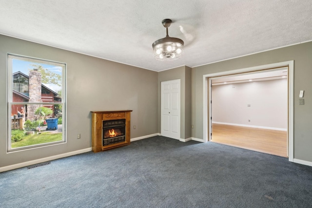 unfurnished living room with dark colored carpet, visible vents, baseboards, a glass covered fireplace, and a textured ceiling