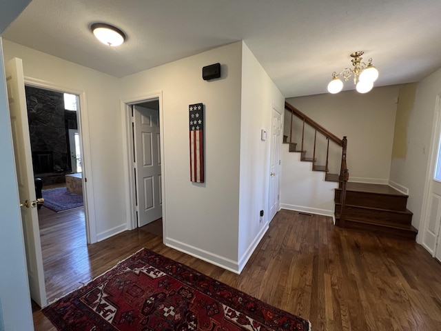 corridor with wood finished floors, an inviting chandelier, baseboards, and stairway