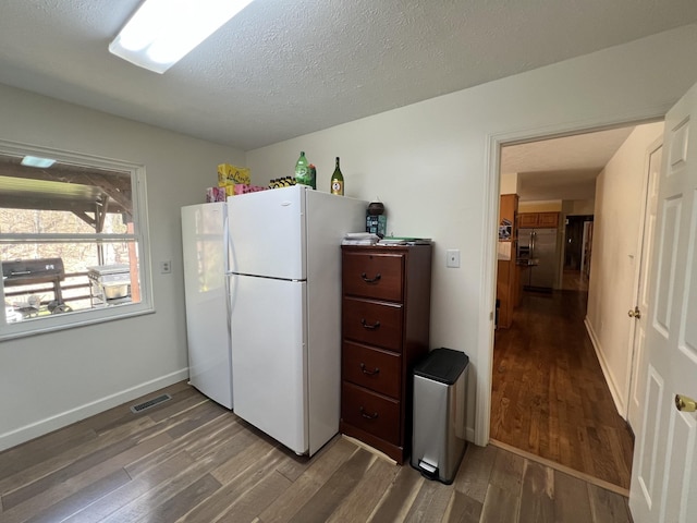 kitchen with baseboards, a textured ceiling, freestanding refrigerator, visible vents, and wood finished floors